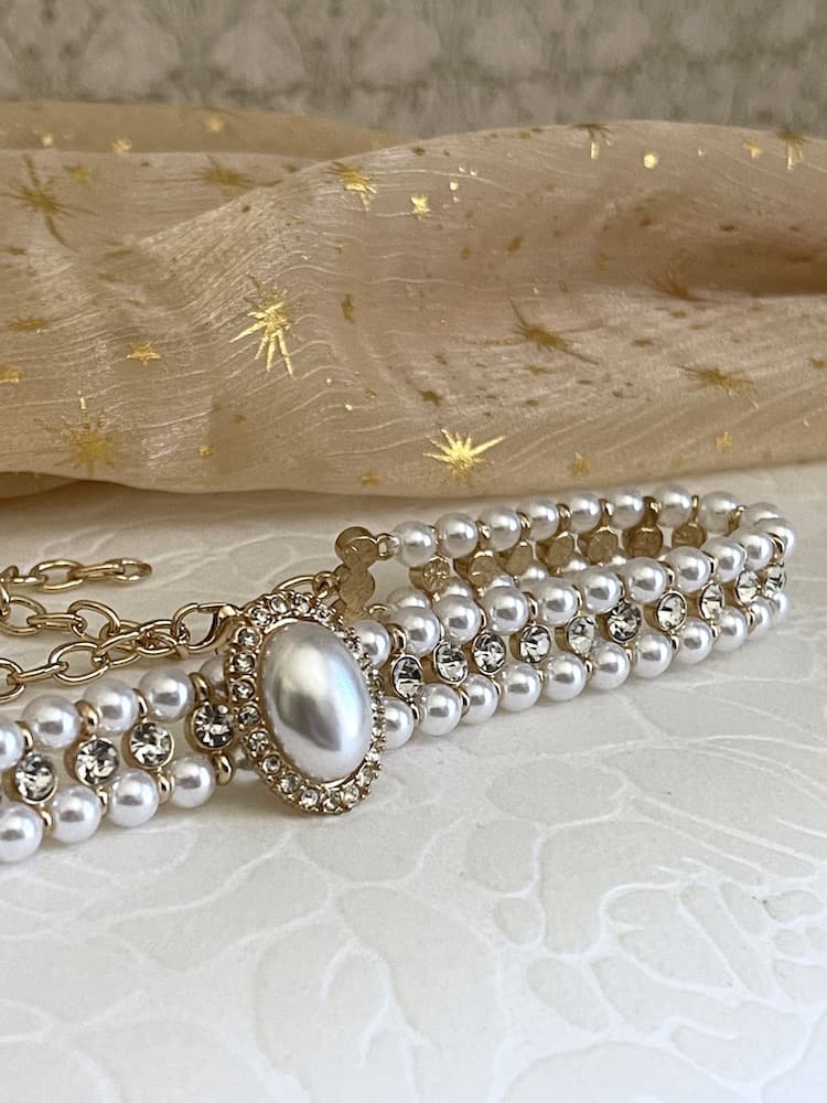A Historically inspired renaissance baroque tudor rococo regency victorian edwardian style pearl and crystal choker necklace is pictured on a floral puff.