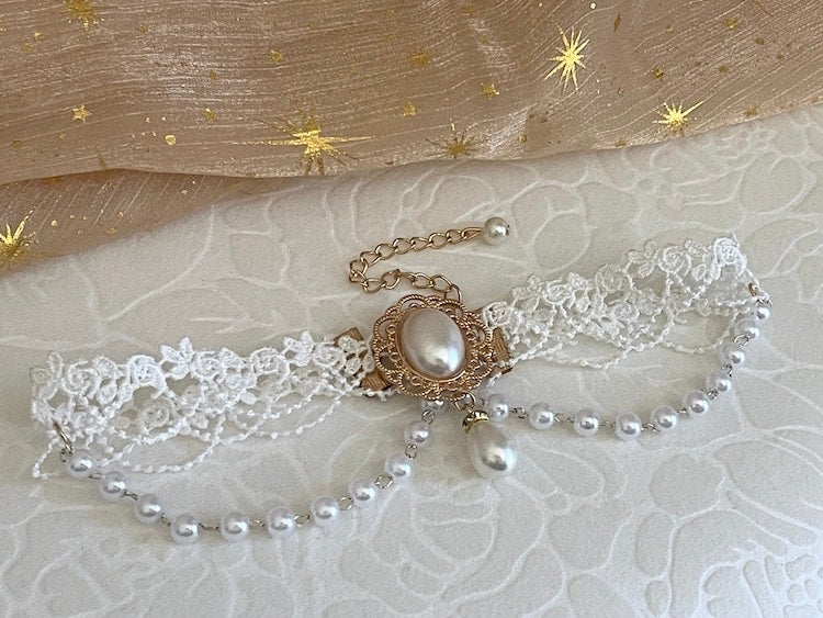 A Rococo or Regency era historically inspired pearl and floral lace choker necklace is pictured on a floral puff.