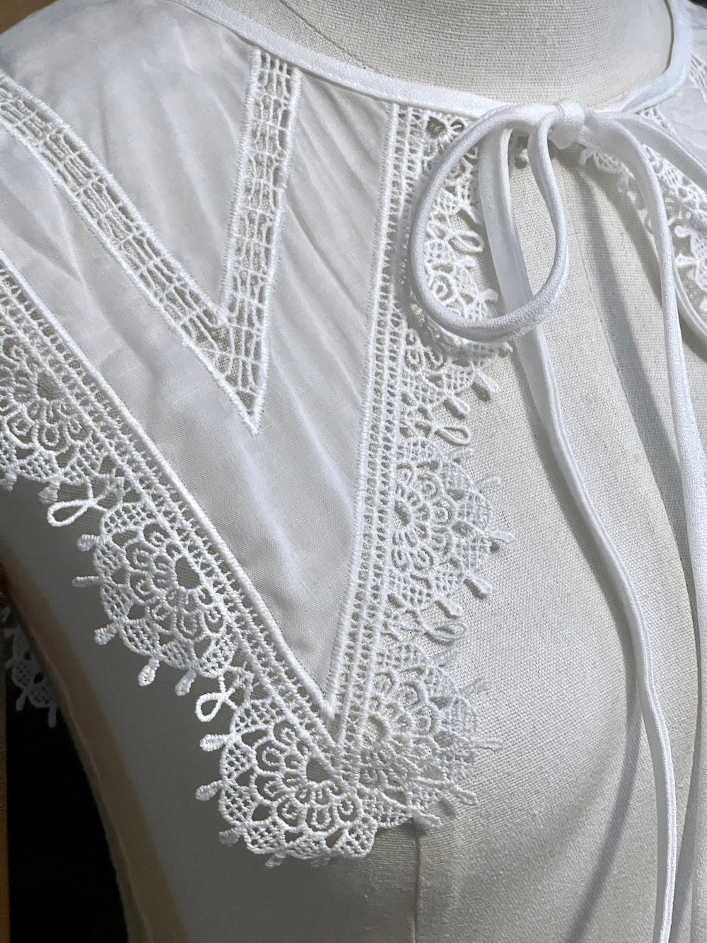 Detail of an Elizabethan era historical fashion inspired white cotton lace trimmed dagger removable collar on a mannequin in front of an art history backdrop.