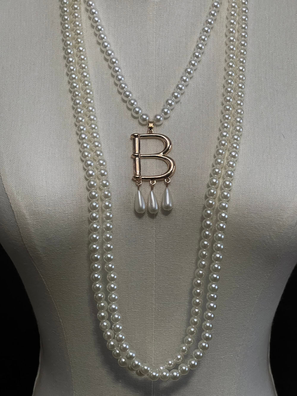 Mannequin wearing a Tudor inspired Anne Boleyn pearl necklace with a decorative 'B' pendant against a dark art history background