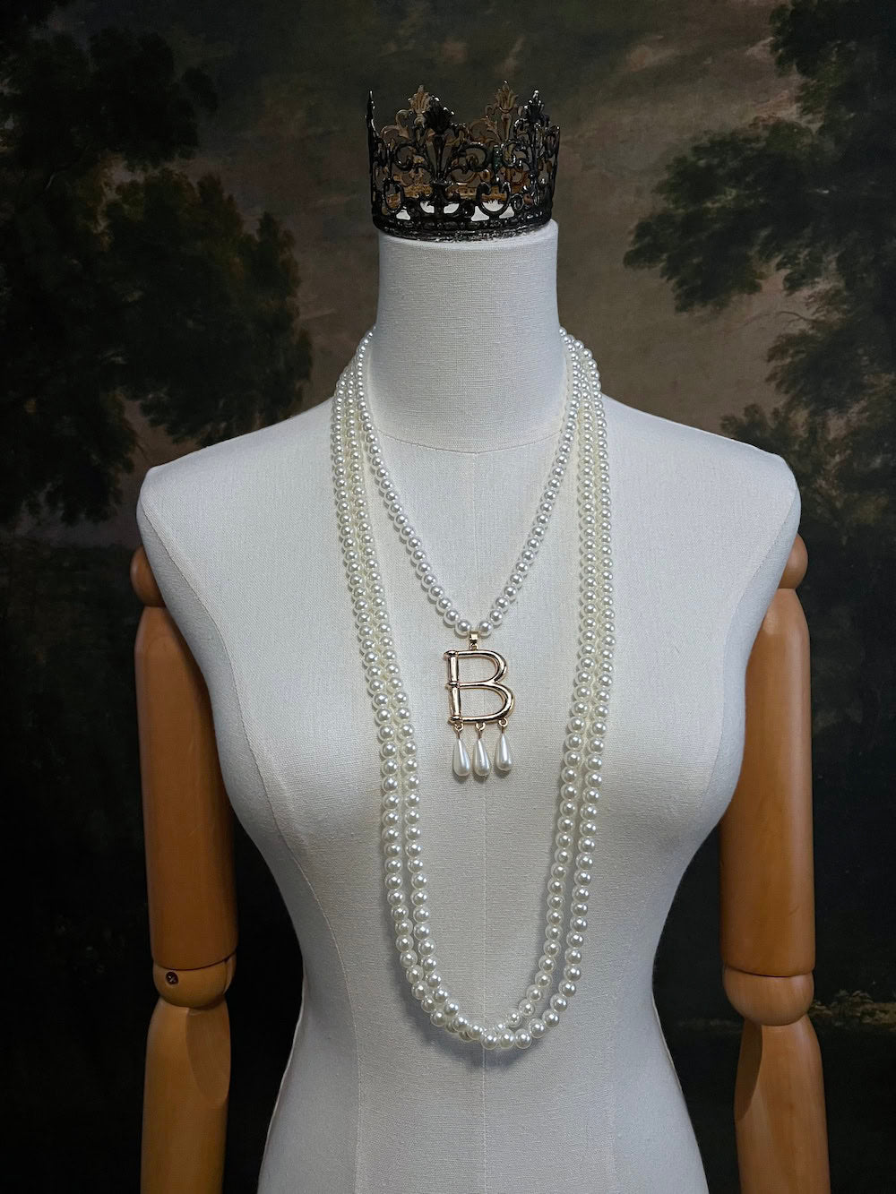 Mannequin wearing a Tudor inspired Anne Boleyn pearl necklace with a decorative 'B' pendant against a dark art history background