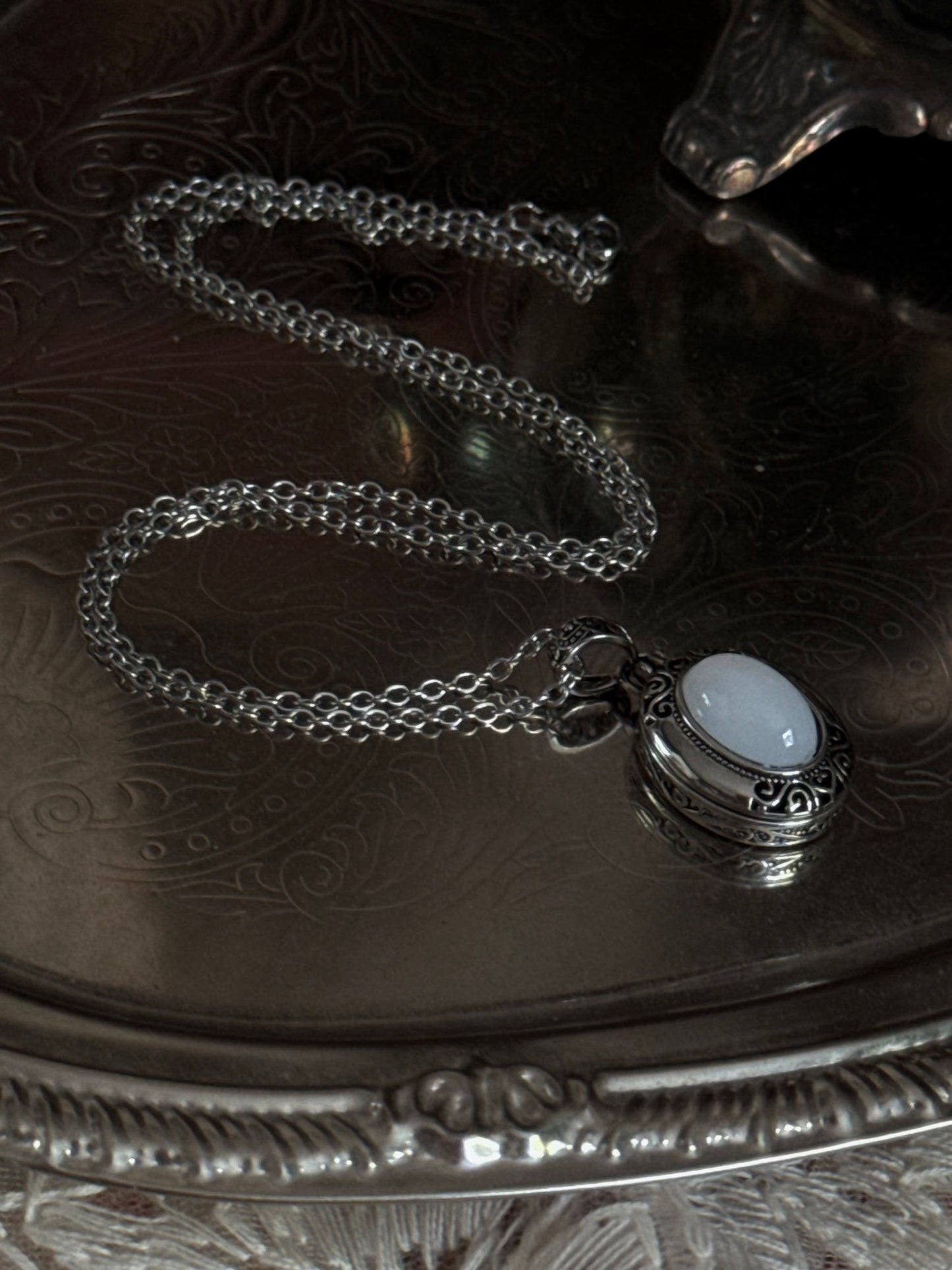 A victorian inspired silverwork locket necklace with filigree designs and a faux moonstone cabochon, pictured on a mannequin