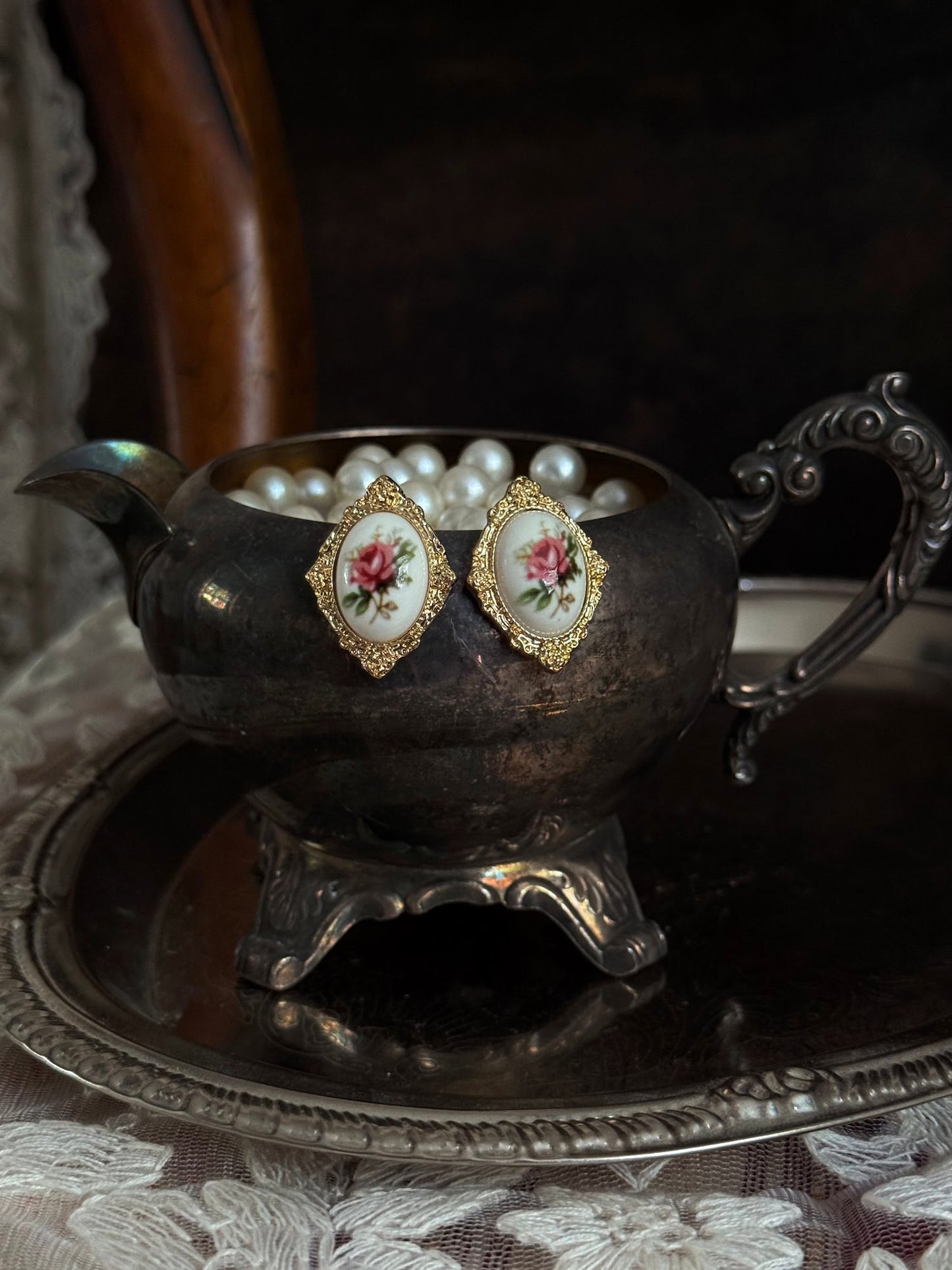 Pair of Historically-Inspired Painted Rose Ceramic gold-framed earrings displayed on an antique silver dish