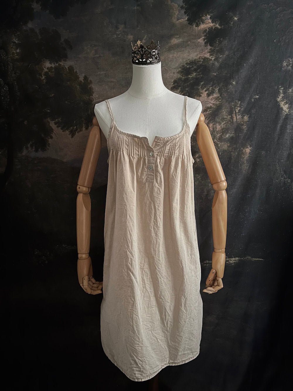 A HISTORICALLY INSPIRED Beige slip chemise dress on a mannequin against a historical painting backdrop.