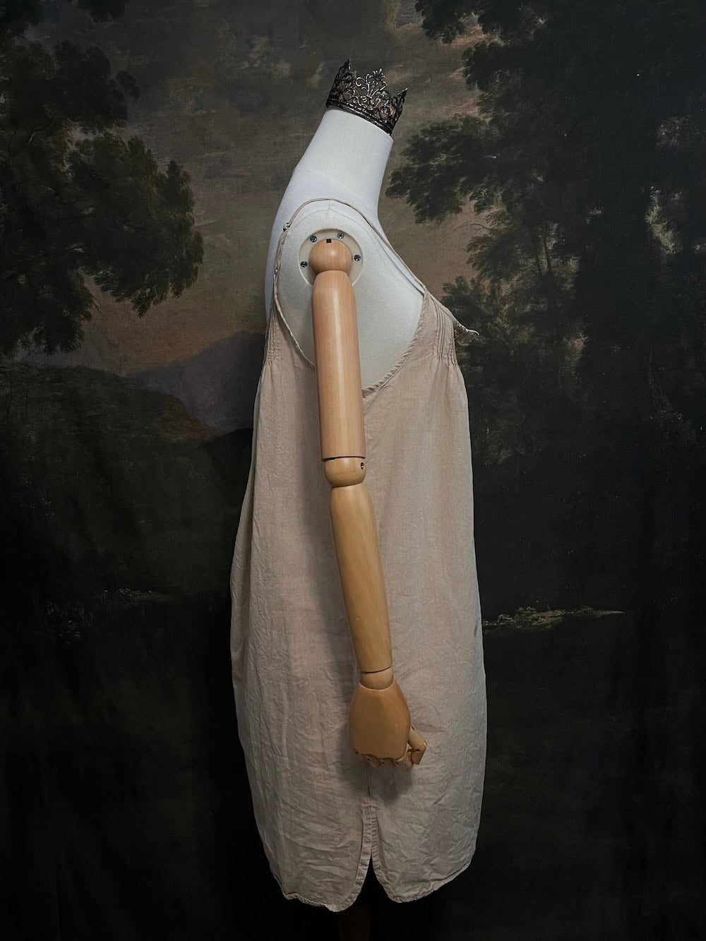 A HISTORICALLY INSPIRED Beige slip chemise dress on a mannequin against a historical painting backdrop.