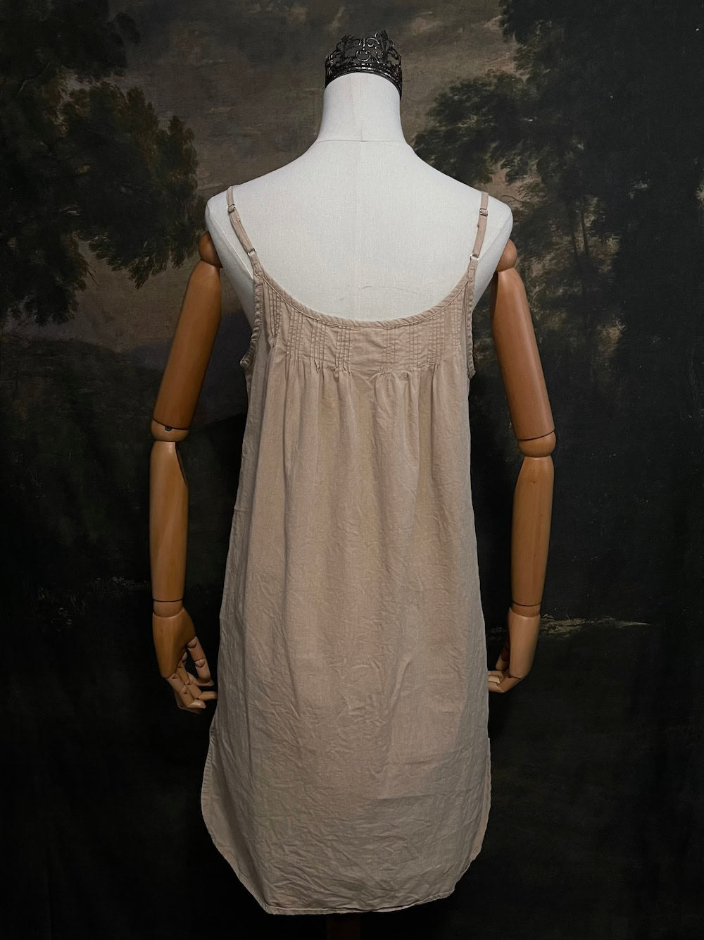 A HISTORICALLY INSPIRED Beige slip chemise dress on a mannequin against a historical painting backdrop.