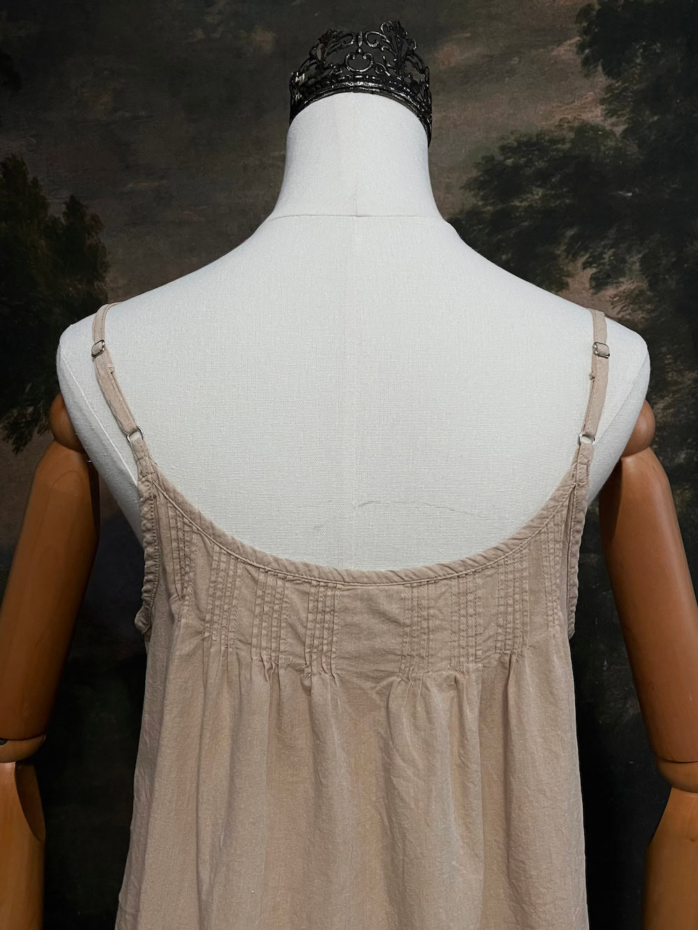 Mannequin wearing a beige smocked dress against a dark, painted background