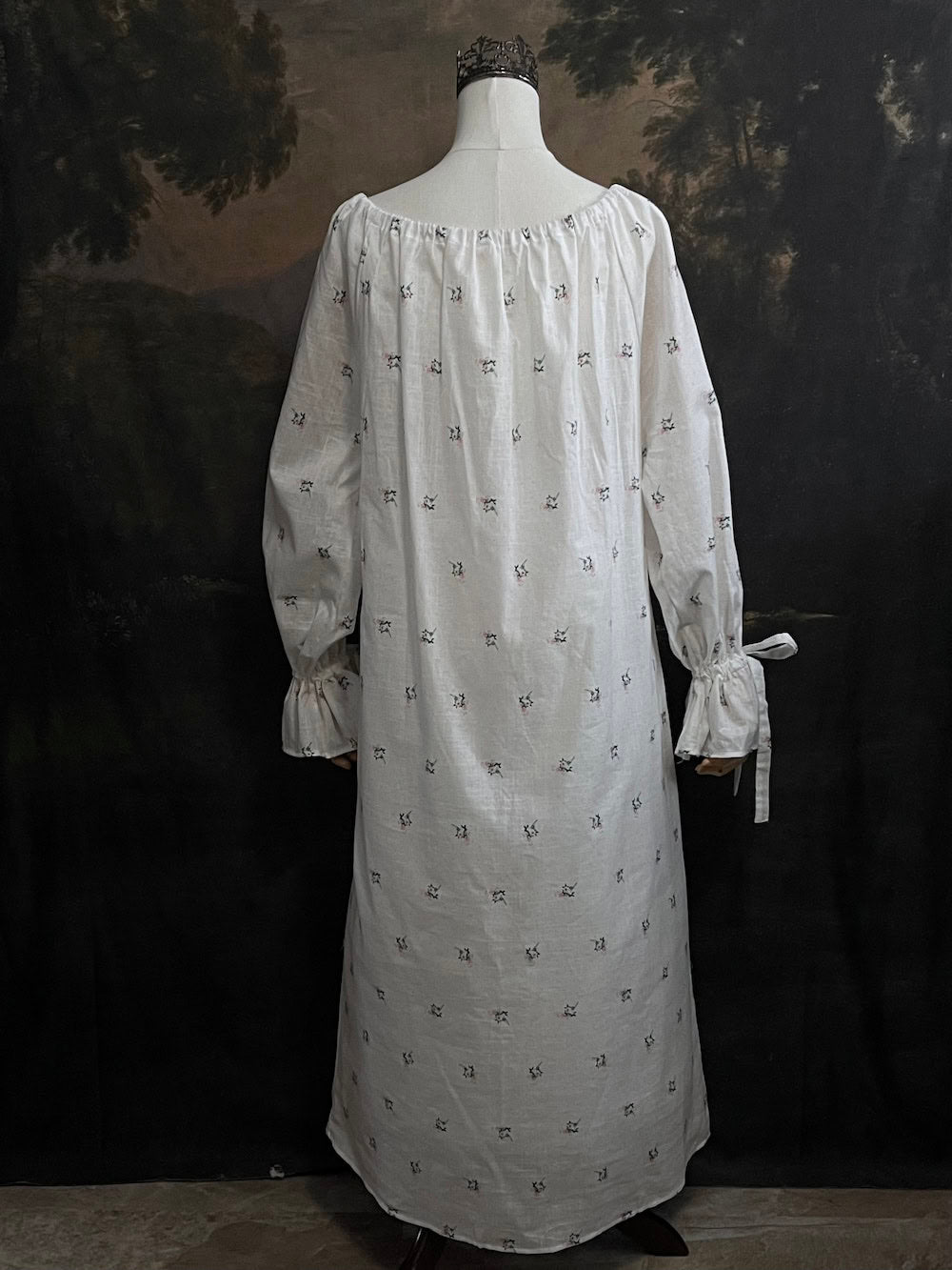 A historically inspired regency and victorian era chemise dress made of white floral printed cotton with bell sleeves and cinched bow neckline
