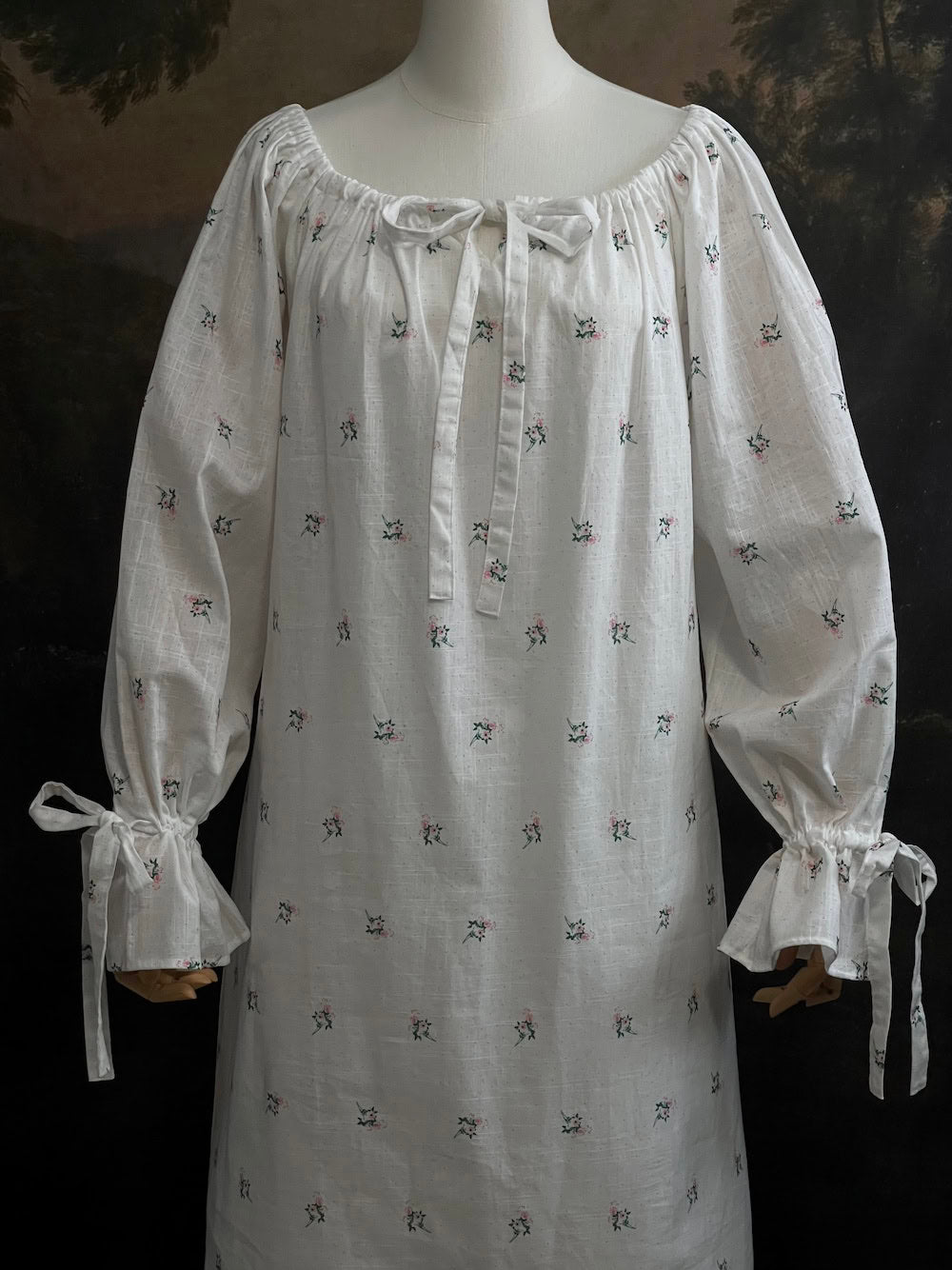 A historically inspired regency and victorian era chemise dress made of white floral printed cotton with bell sleeves and cinched bow neckline