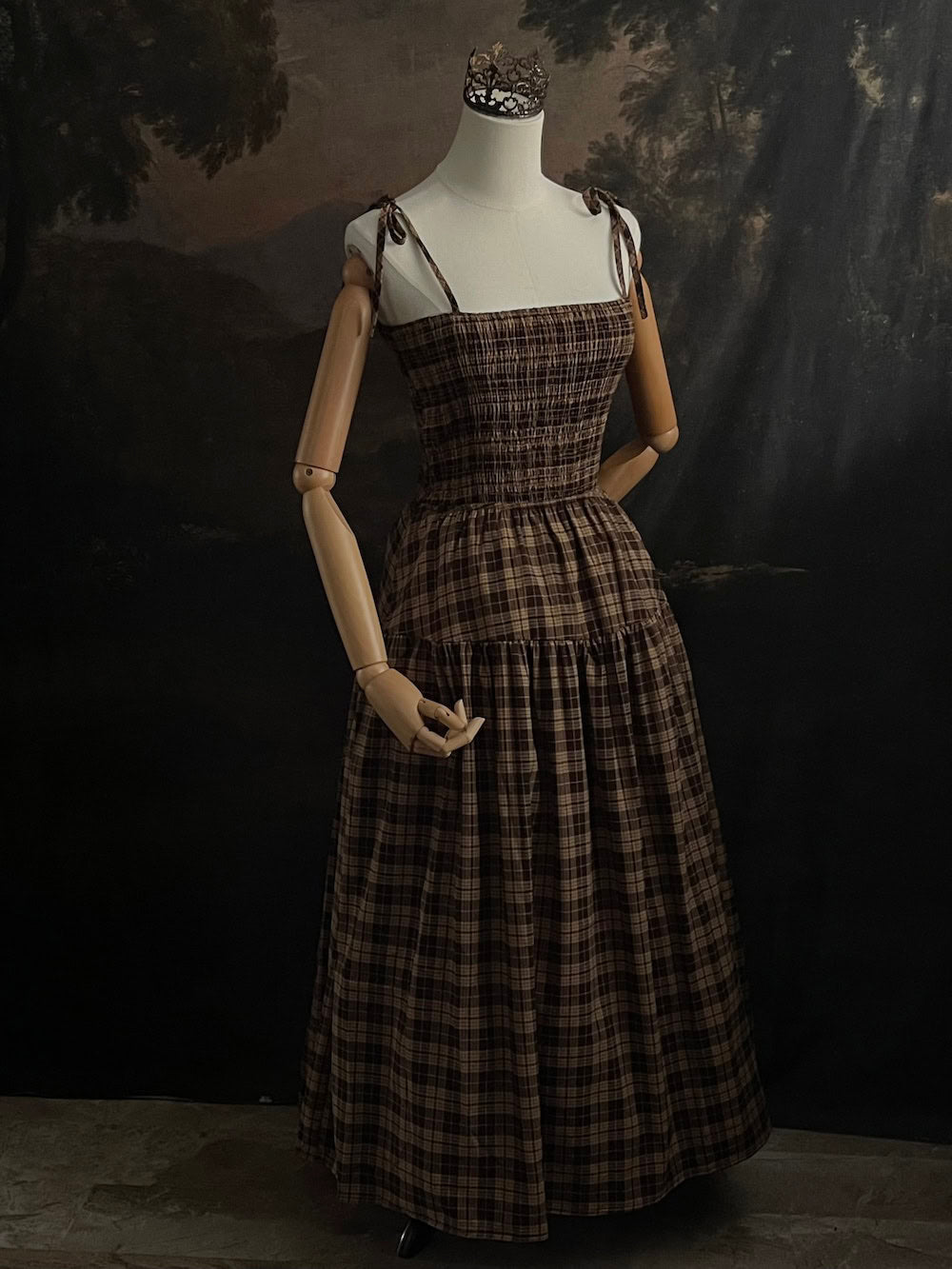 Mannequin wearing a historical fashion inspired brown tartan plaid maxi dress against a dark art history background
