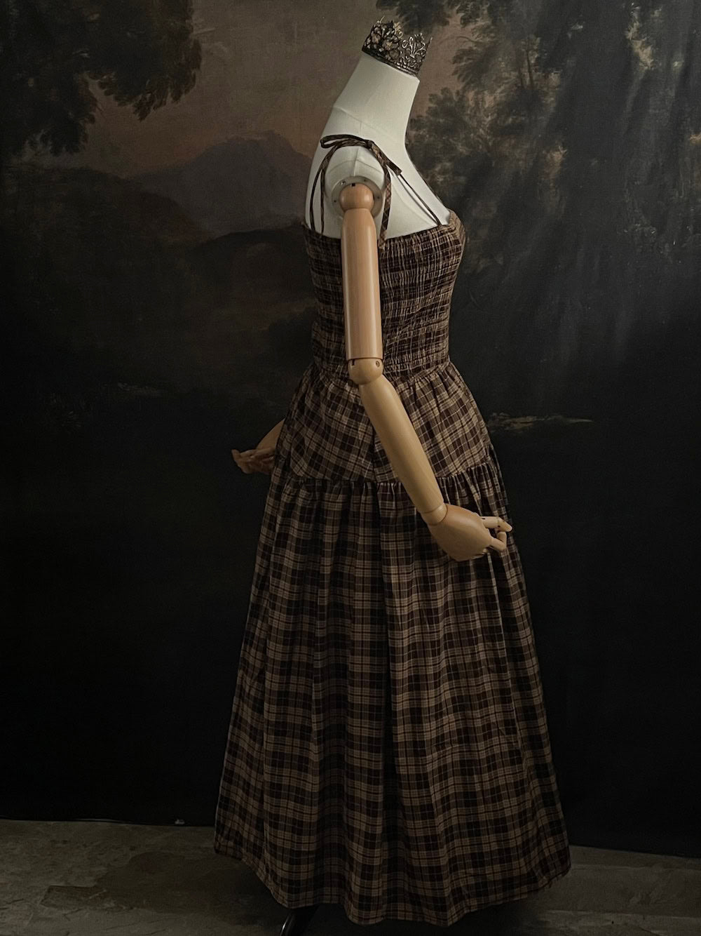 Mannequin wearing a historical fashion inspired brown tartan plaid maxi dress against a dark art history background