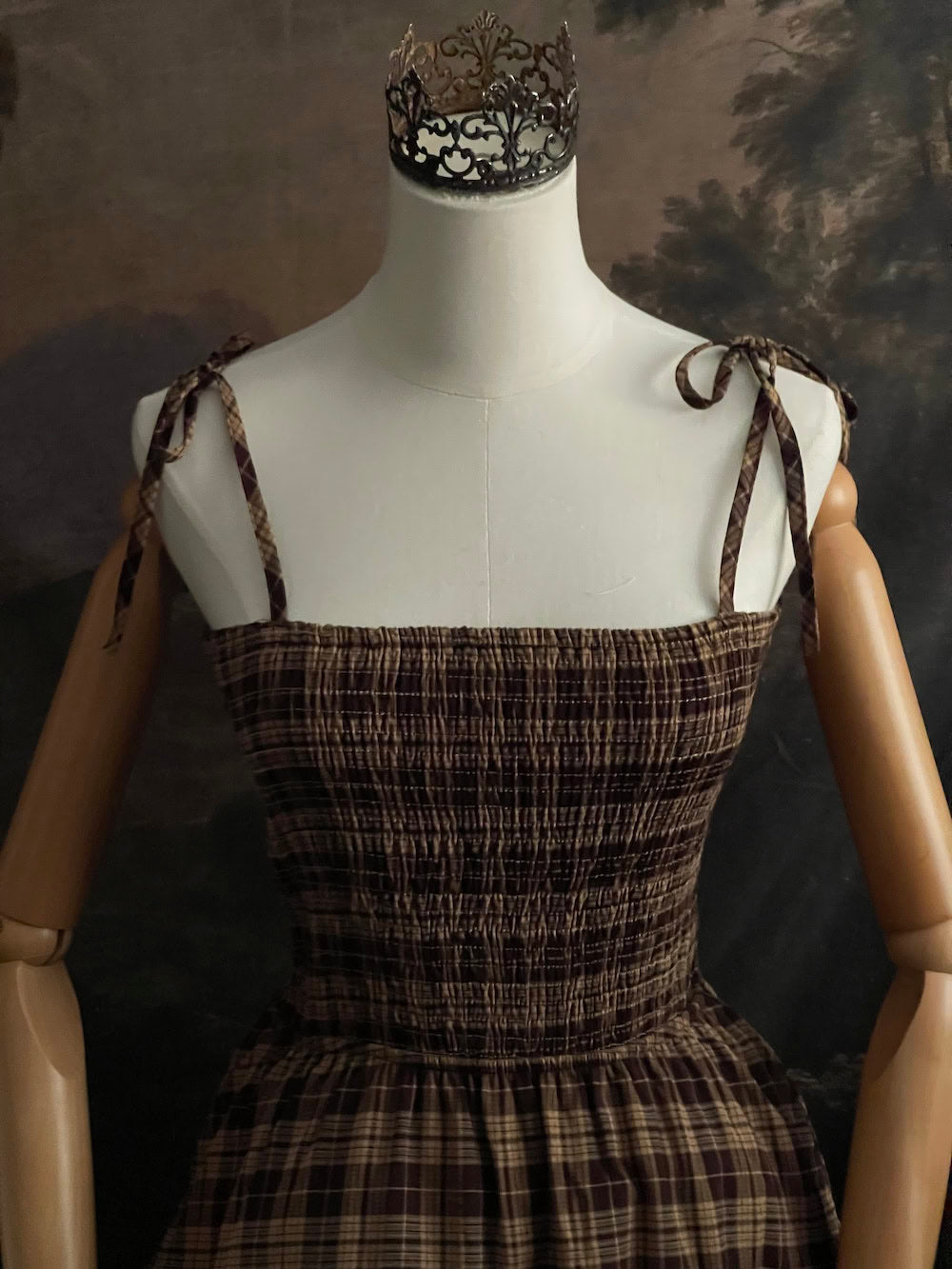 Up close of a Mannequin wearing a historical fashion inspired brown tartan plaid maxi dress against a dark art history background