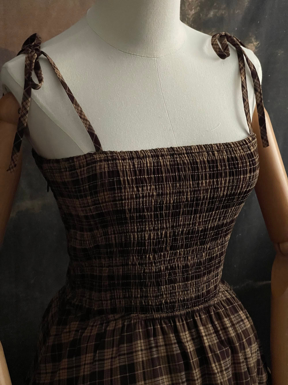 Up close of a Mannequin wearing a historical fashion inspired brown tartan plaid maxi dress against a dark art history background