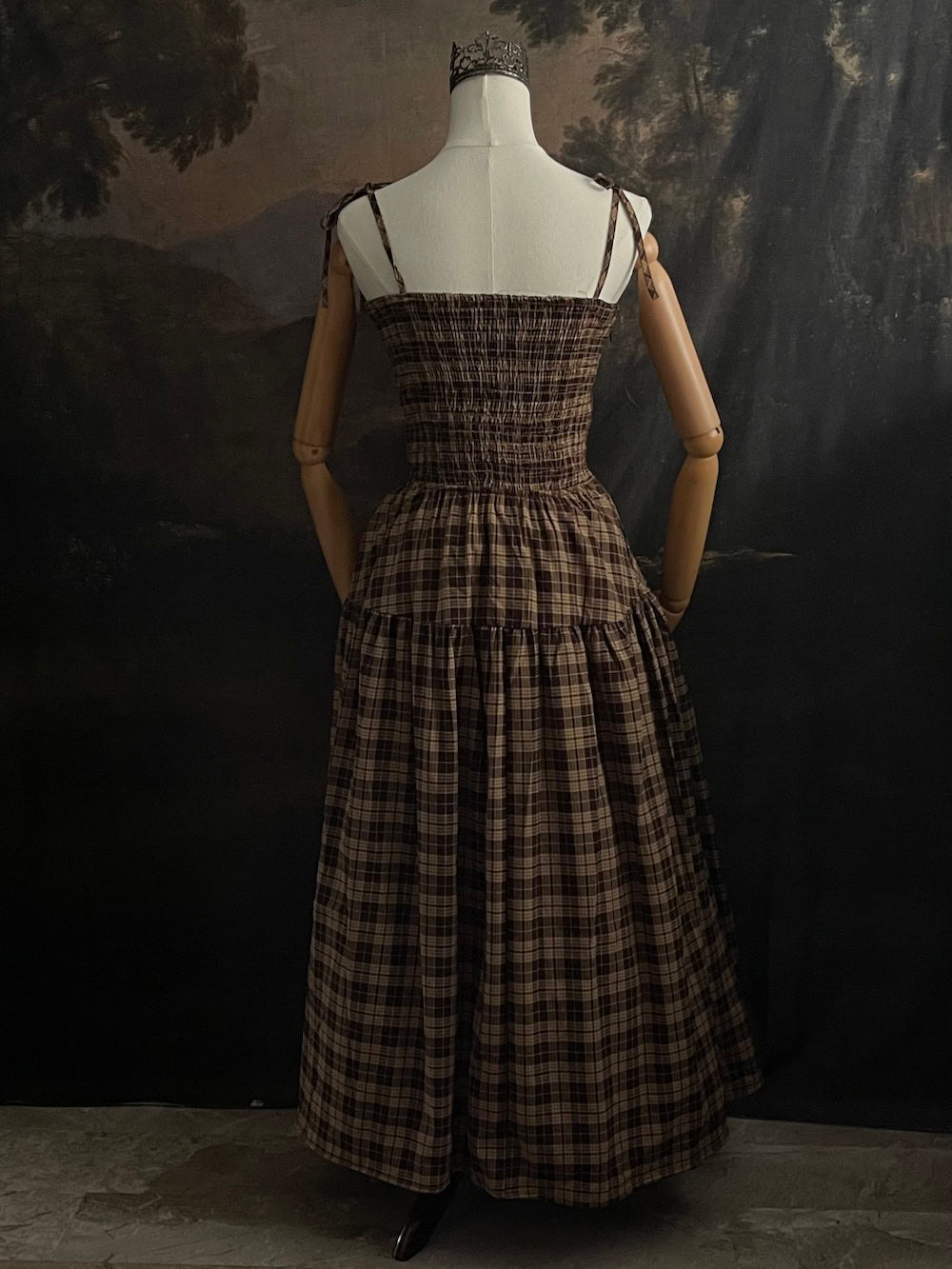 Mannequin wearing a historical fashion inspired brown tartan plaid maxi dress against a dark art history background