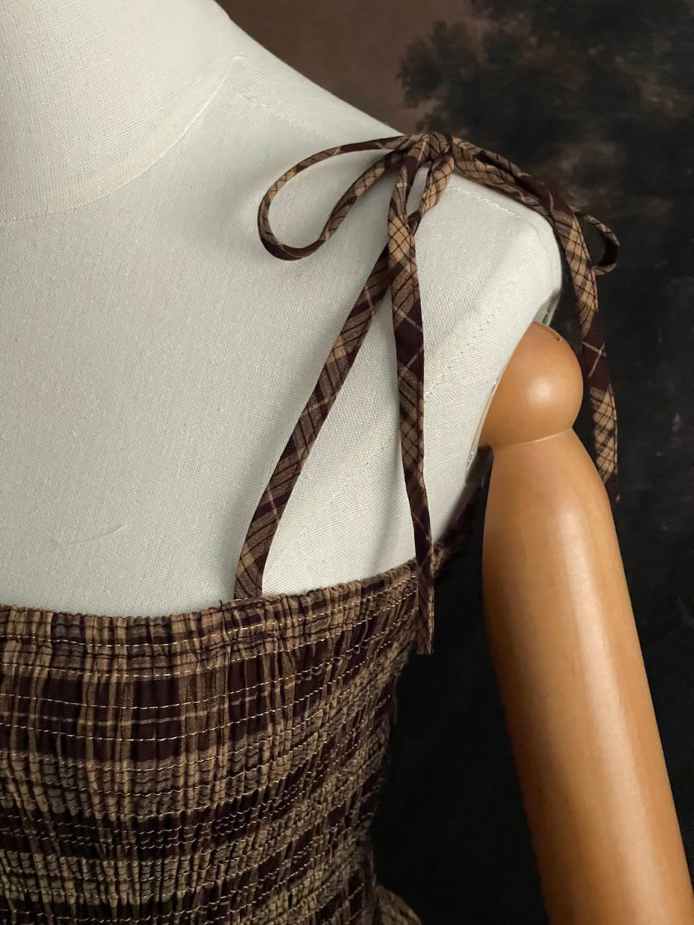up close detail of Mannequin wearing a historical fashion inspired brown tartan plaid maxi dress against a dark art history background