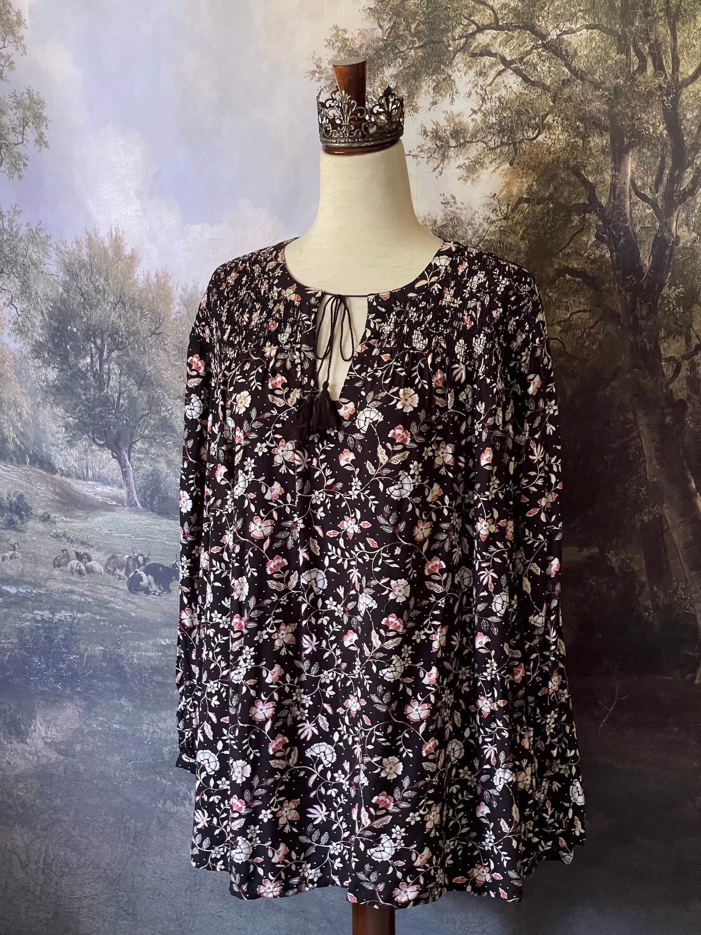 A Medieval Inspired Dark Botanical Print Blouse with Bishop Sleeves on a mannequin in front of a forested painting backdrop.