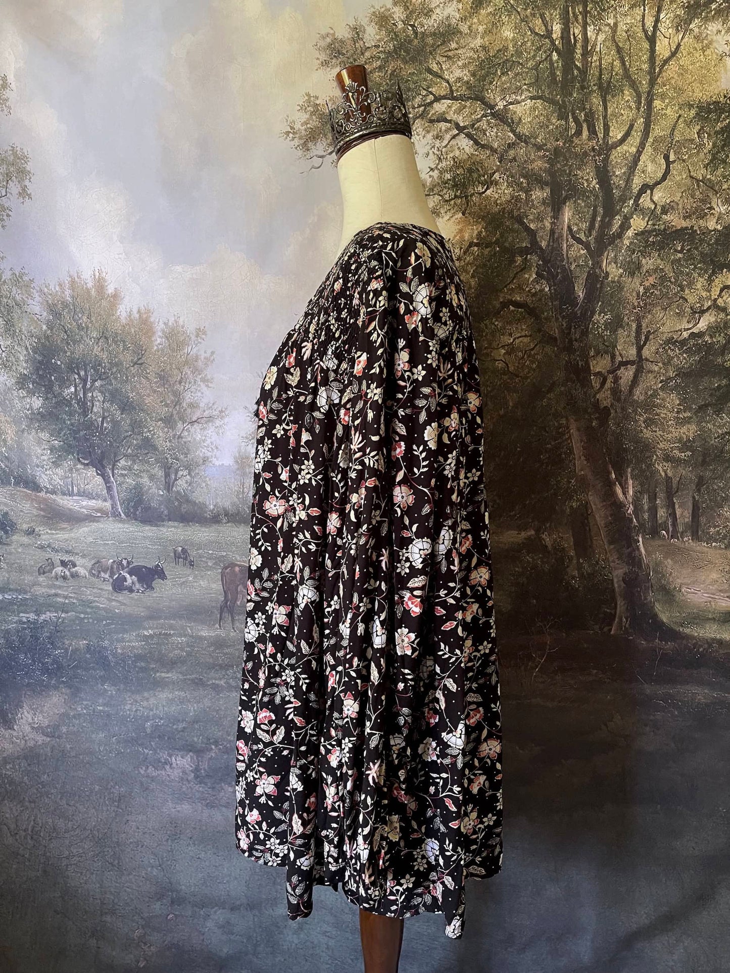 A Medieval Inspired Dark Botanical Print Blouse with Bishop Sleeves on a mannequin in front of a forested painting backdrop.
