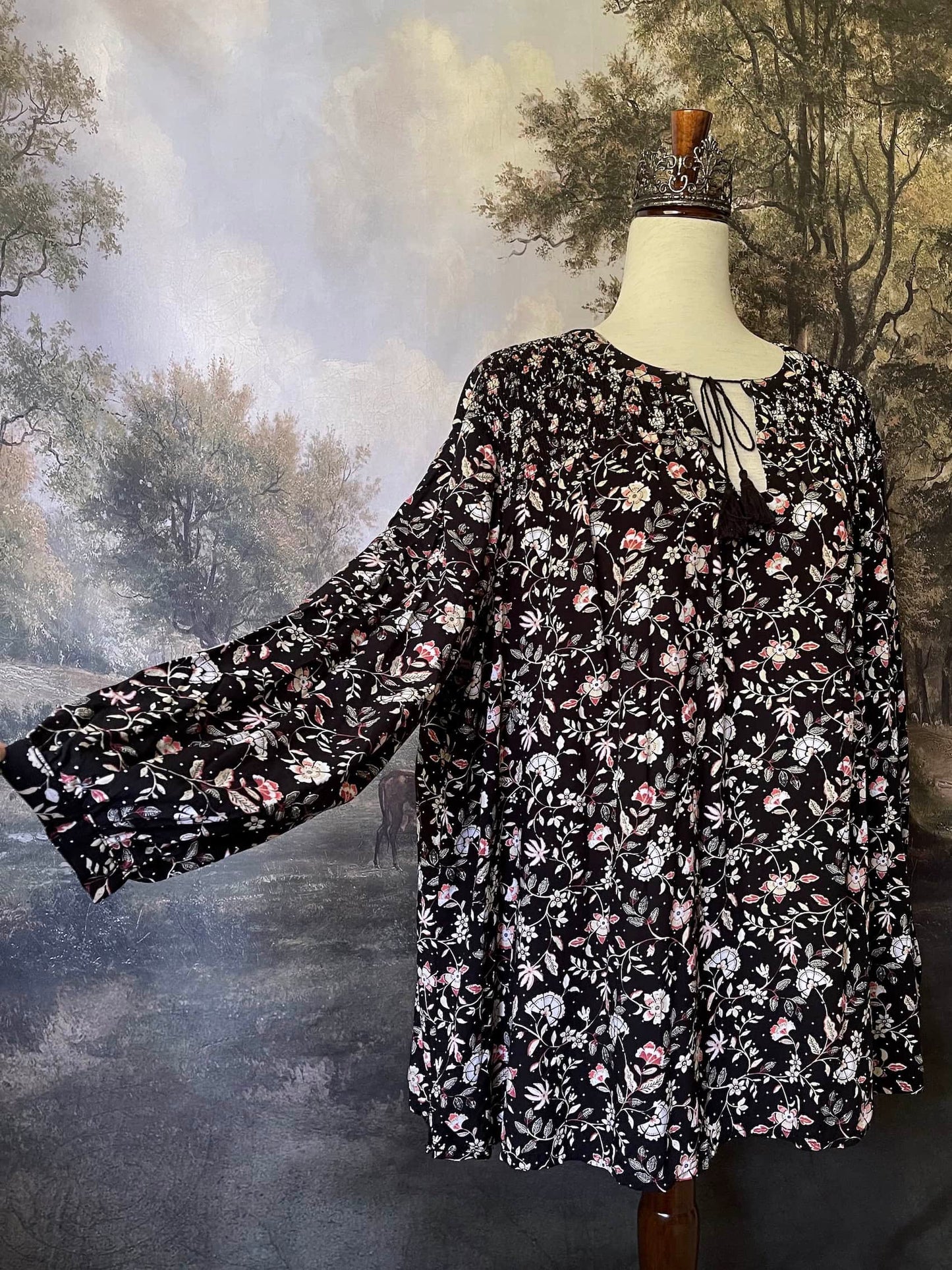 A Medieval Inspired Dark Botanical Print Blouse with Bishop Sleeves on a mannequin in front of a forested painting backdrop.
