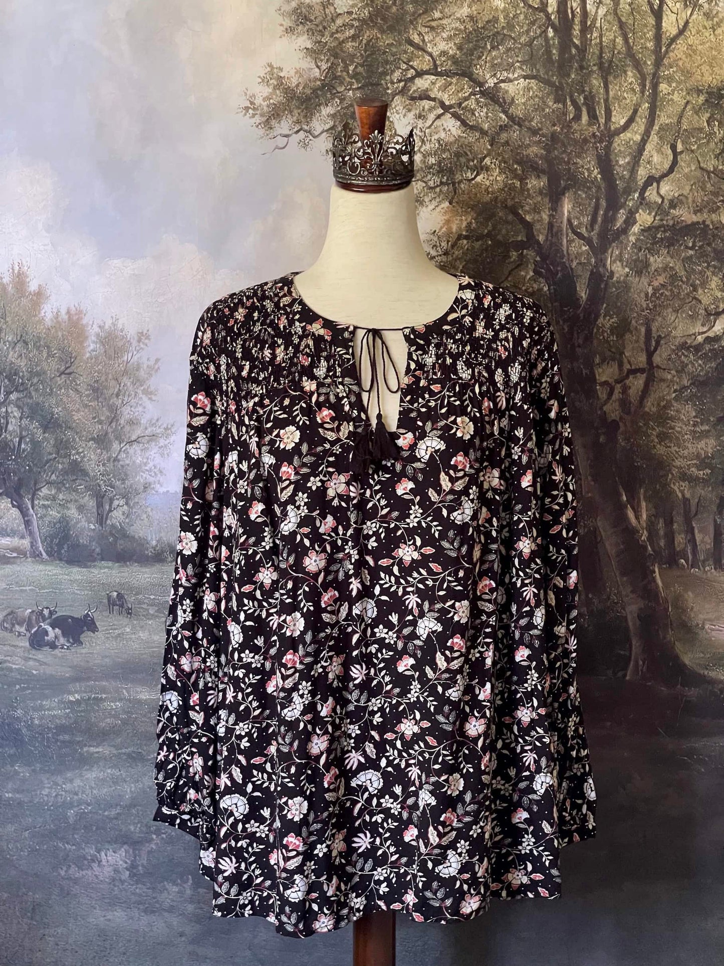 A Medieval Inspired Dark Botanical Print Blouse with Bishop Sleeves on a mannequin in front of a forested painting backdrop.