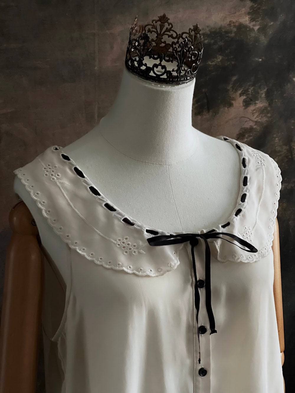 close up of off-white vintage style peter-pan collar blouse with black ribbon bow details on a mannequin against a dark art history background