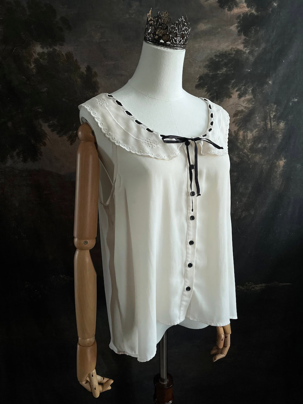 off-white vintage style peter-pan collar blouse with black ribbon bow details on a mannequin against a dark art history background