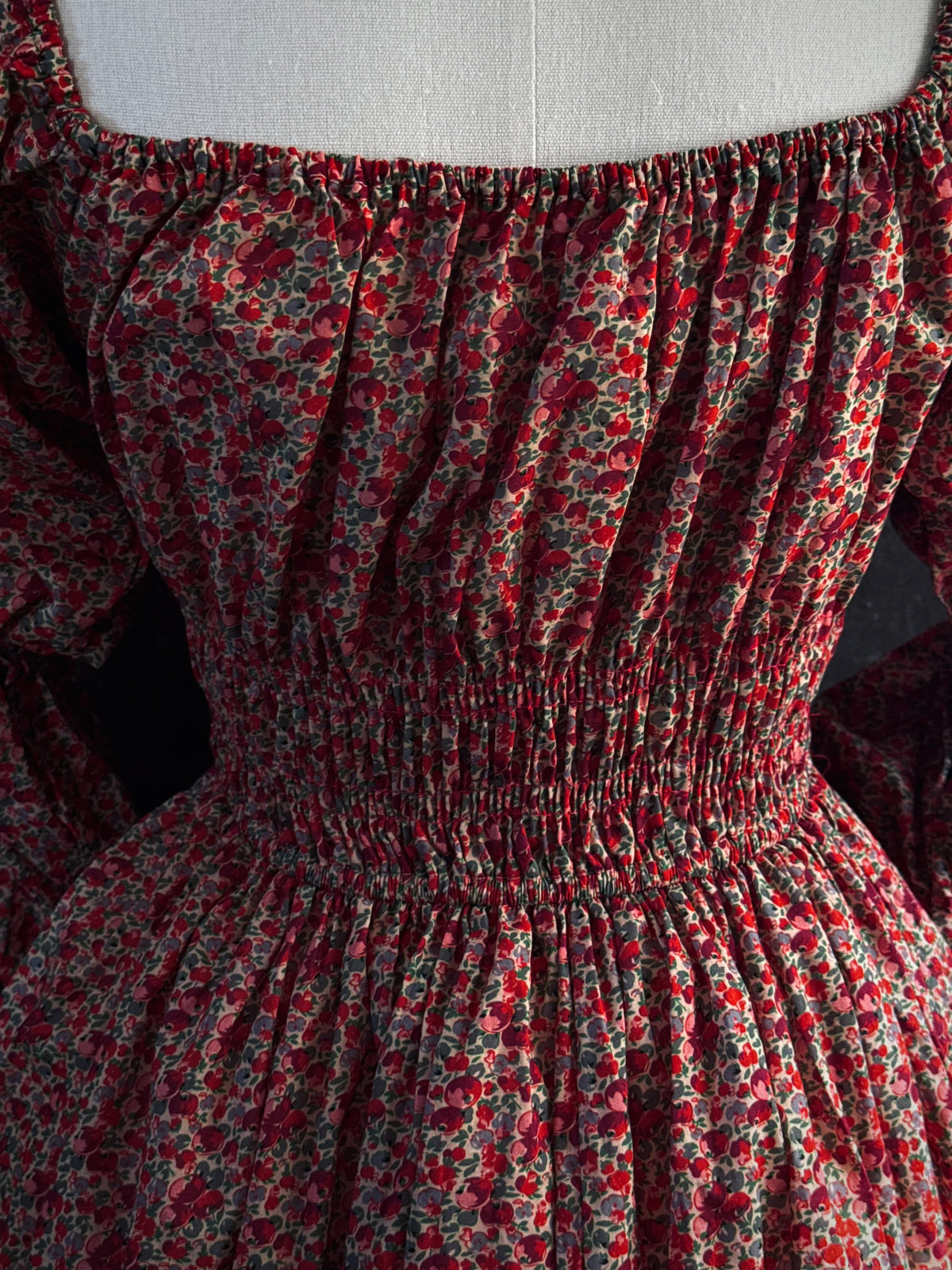 Close-up of a smocked dress with a red and green apple print, featuring a square neckline and gathered waist.