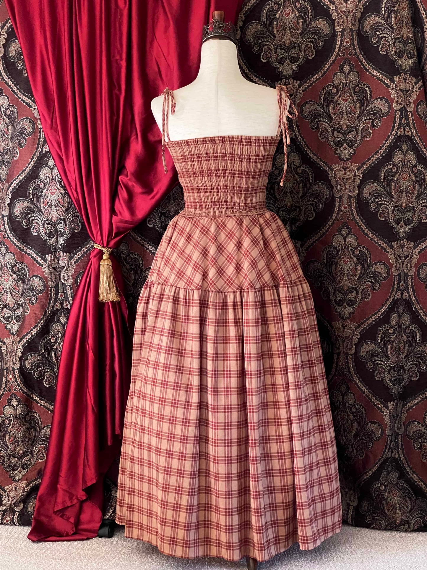 An early medieval era, Anglo Saxon, historically inspired rust and burgundy tartan plaid smocked maxi dress with tiered skirt pictured on a mannequin.