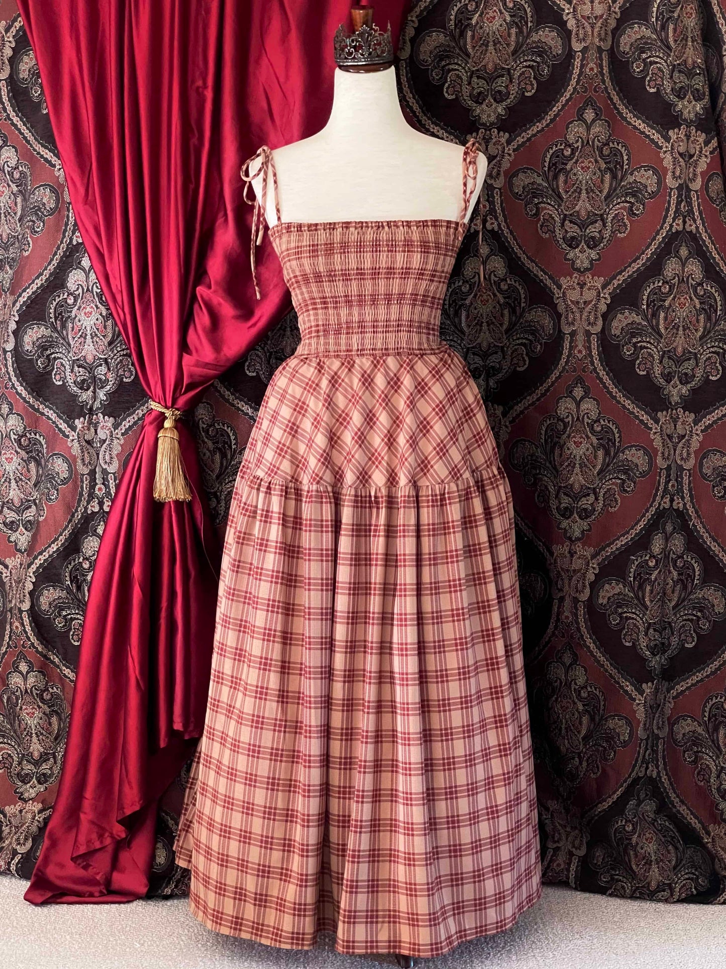 An early medieval era, Anglo Saxon, historically inspired rust and burgundy tartan plaid smocked maxi dress with tiered skirt pictured on a mannequin.
