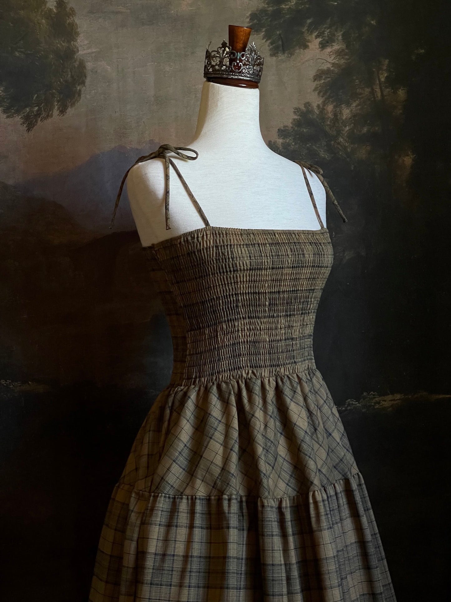 An early medieval era, Celtic historically inspired olive green tartan plaid smocked maxi dress with tiered skirt pictured on a mannequin.