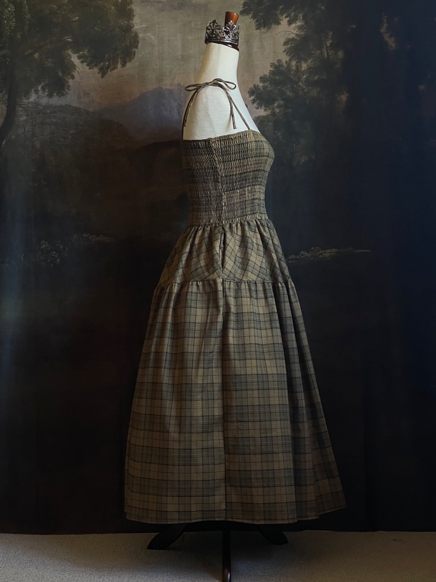 An early medieval era, Celtic historically inspired olive green tartan plaid smocked maxi dress with tiered skirt pictured on a mannequin.