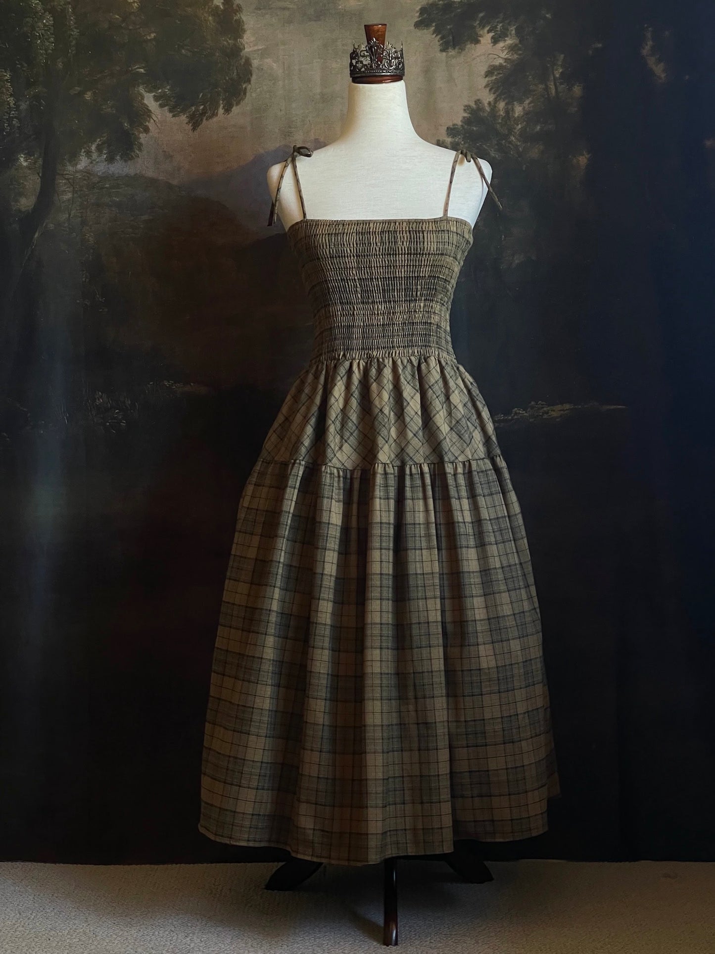An early medieval era, Celtic historically inspired olive green tartan plaid smocked maxi dress with tiered skirt pictured on a mannequin.