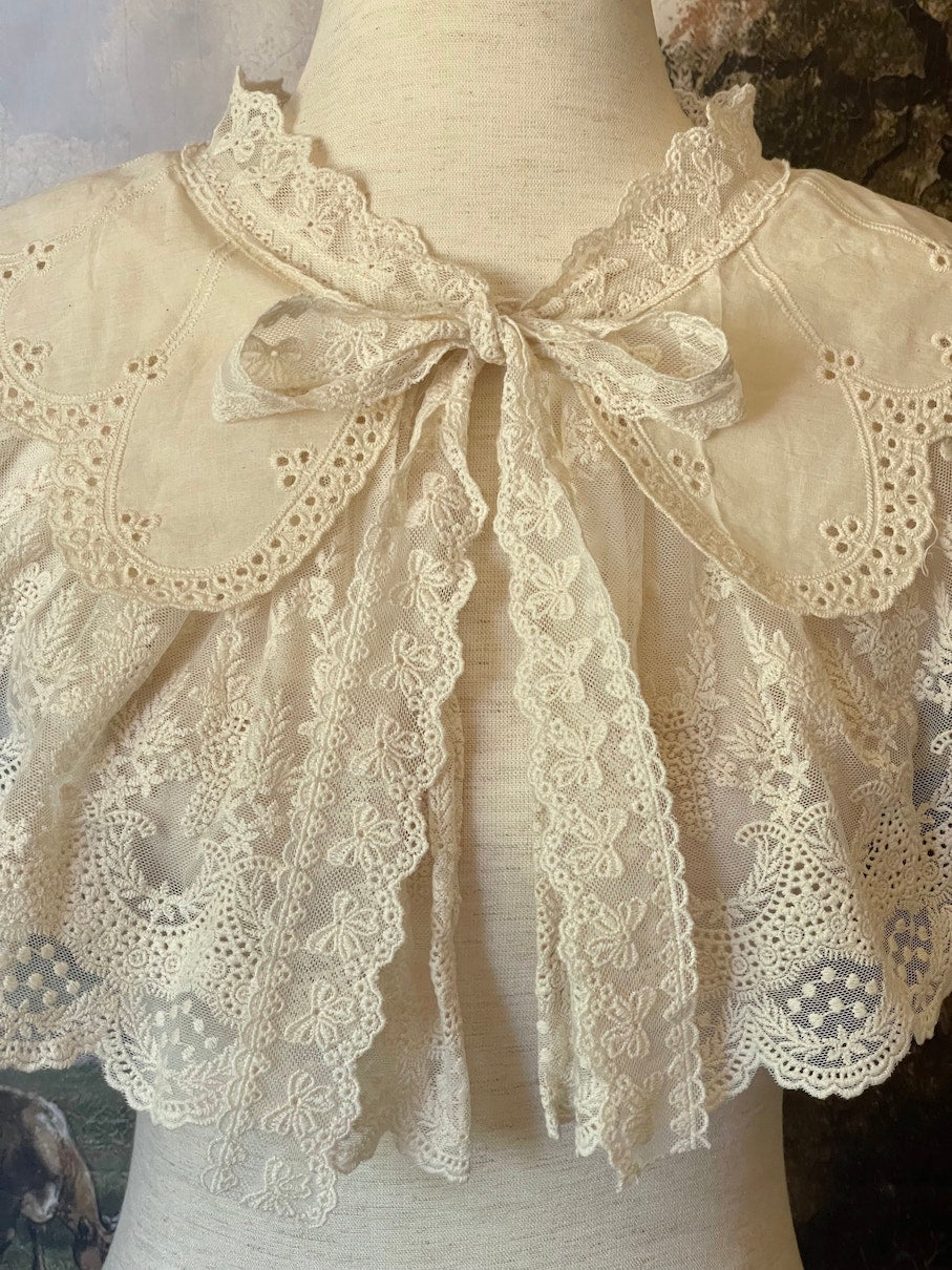 A Historically inspired edwardian victorian regency and rococo style lace capelet shawl in ivory with bow and floral embroidered details.