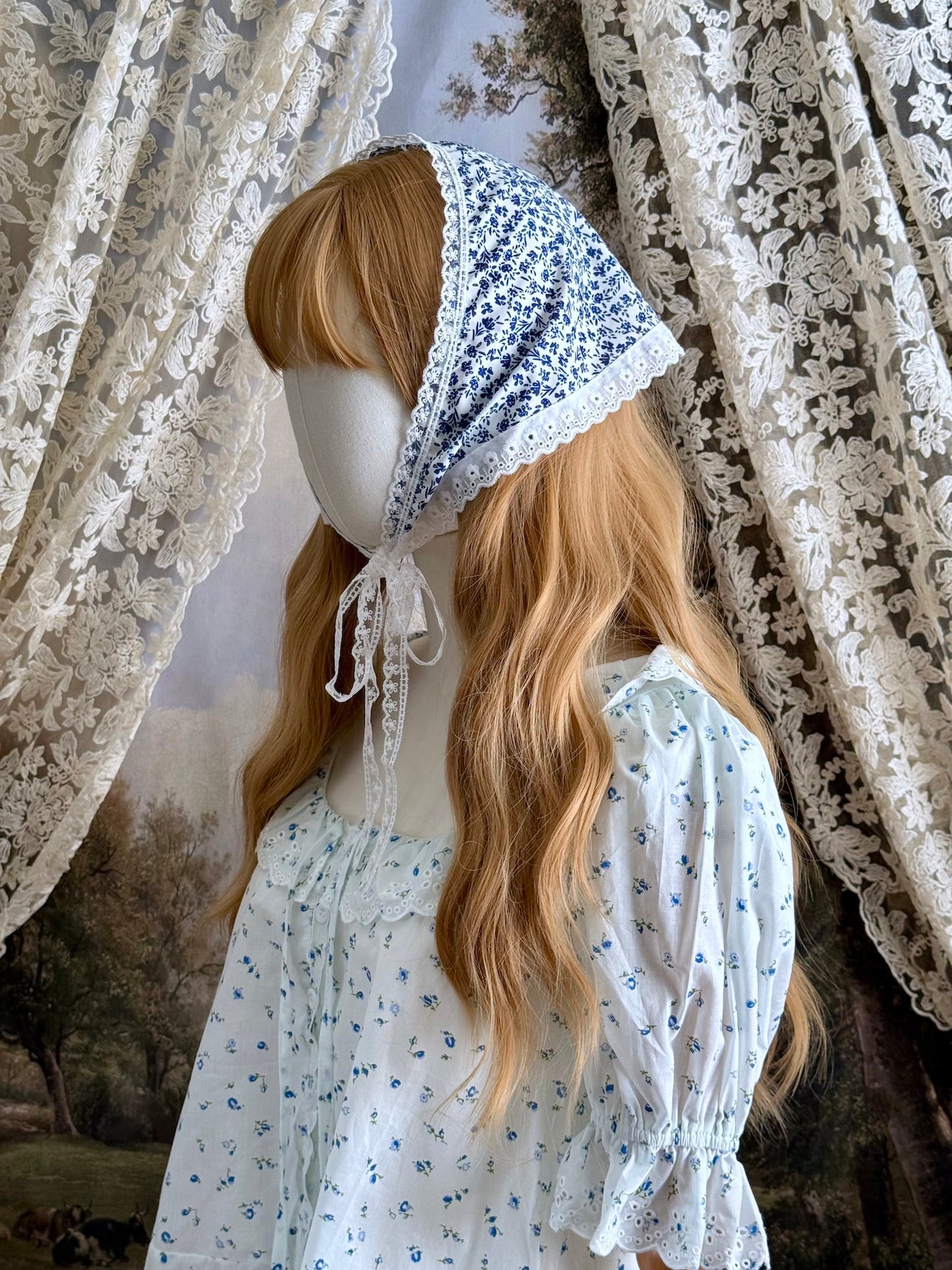 A vintage style historically inspired blue and white floral print babushka triangle headdress with floral lace trim pictured on a mannequin.