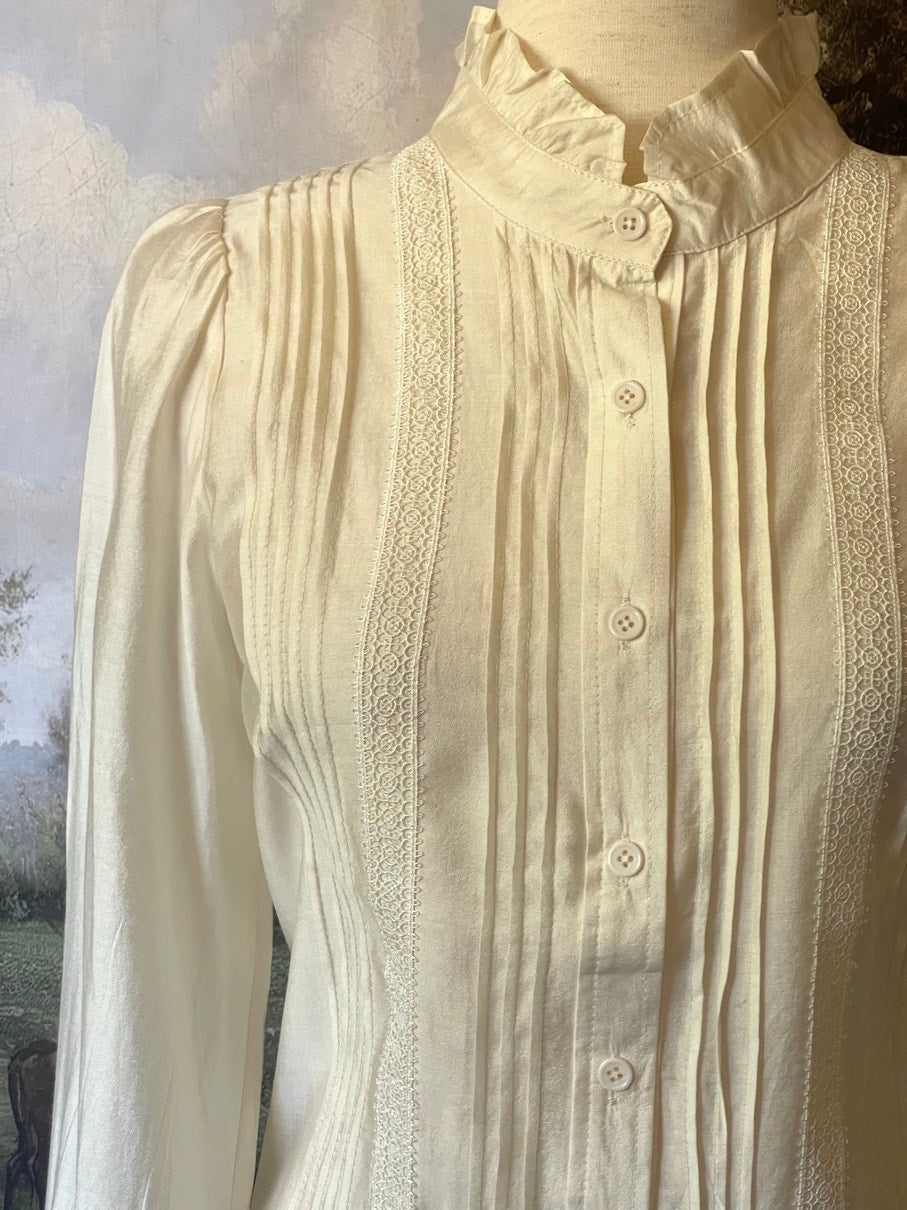 A historically inspired victorian and edwardian era style ivory colored blouse with pintucks, a high neck collar, ruffle hem sleeves, and crochet lace.