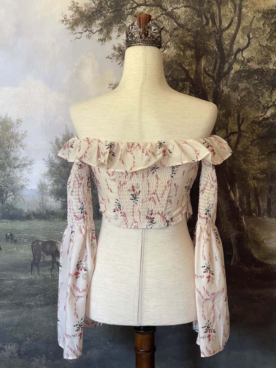 A historically inspired off-shoulder ruffle neckline floral print blouse with bell sleeves and a structured corset-like bodice.