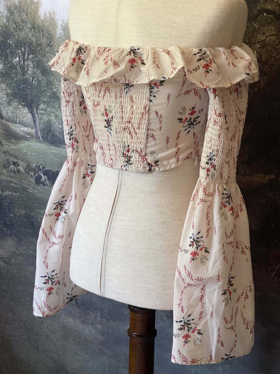 A historically inspired off-shoulder ruffle neckline floral print blouse with bell sleeves and a structured corset-like bodice.
