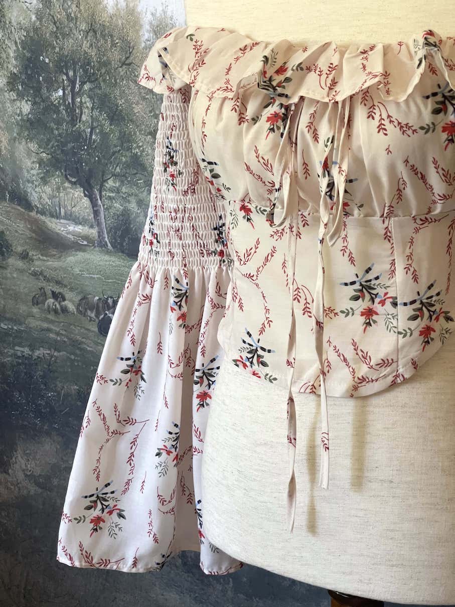 A historically inspired off-shoulder ruffle neckline floral print blouse with bell sleeves and a structured corset-like bodice.