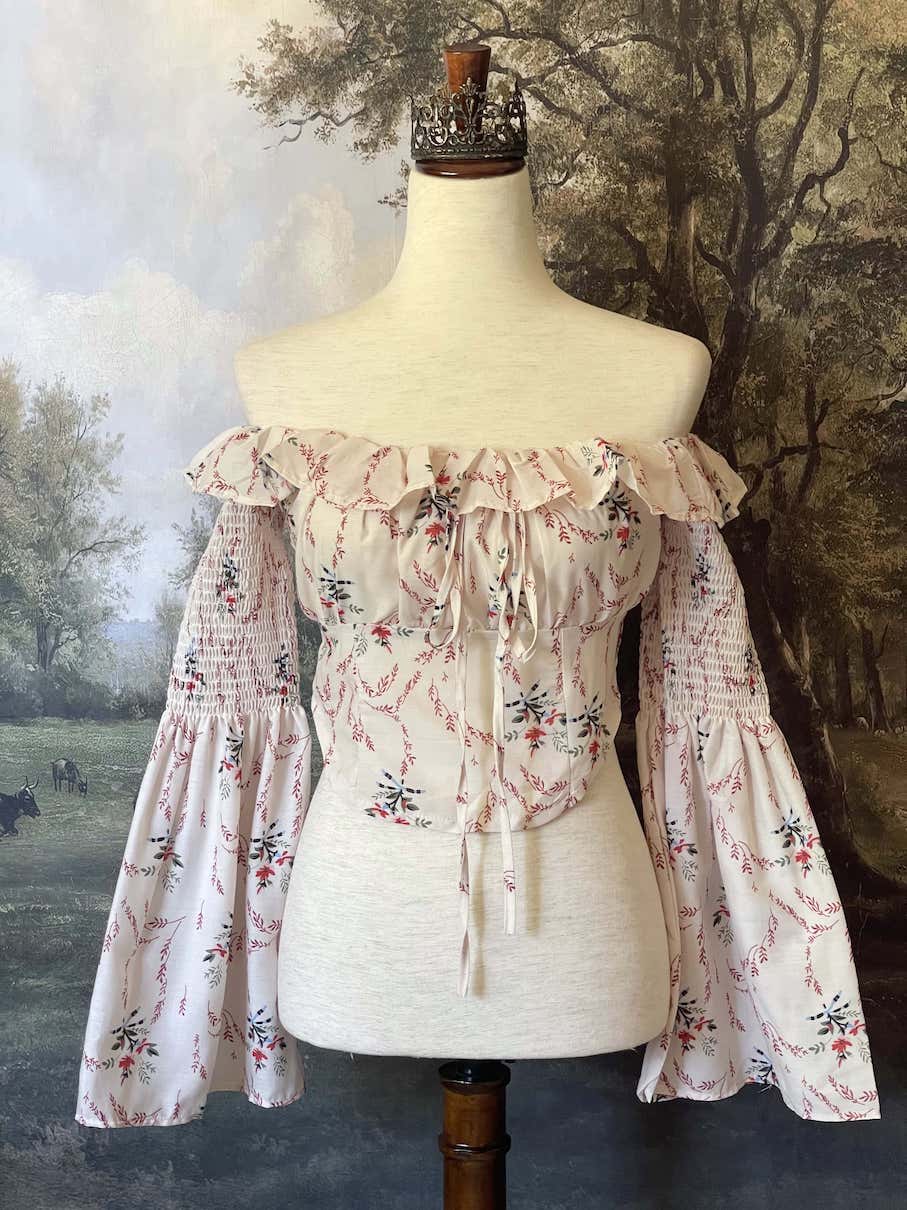 A historically inspired off-shoulder ruffle neckline floral print blouse with bell sleeves and a structured corset-like bodice.