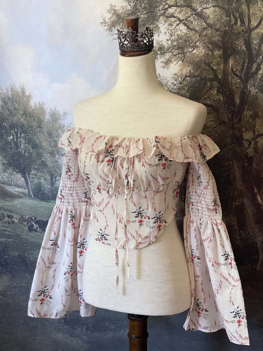 A historically inspired off-shoulder ruffle neckline floral print blouse with bell sleeves and a structured corset-like bodice.