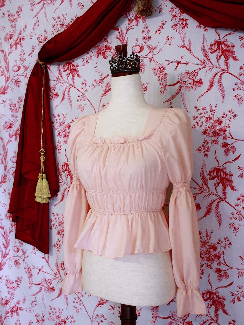 Historically Inspired Renaissance Smocked Blouse with Juliet Puff Sleeves in Peachy Pink, in front of a toile backdrop.