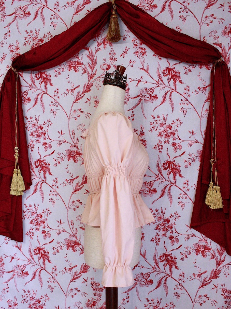 Historically Inspired Renaissance Smocked Blouse with Juliet Puff Sleeves in Peachy Pink, in front of a toile backdrop.