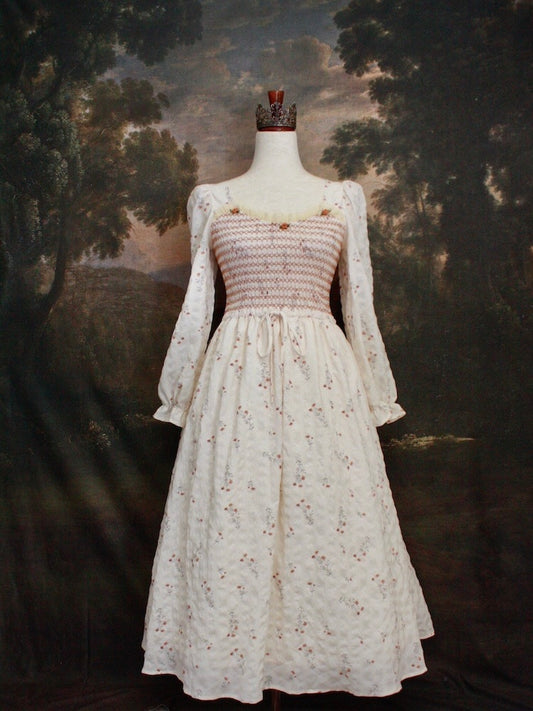 A Historically inspired rococo and regency Ivory bishop sleeve smocked tea gown with peach contrast stitching is pictured on a mannequin in front of a historical painting backdrop.