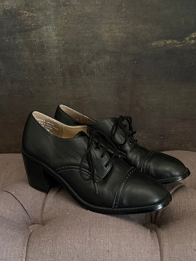 Vintage 90s y2k historically inspired black leather oxford heels with lace up detail, in front of historical painting background.