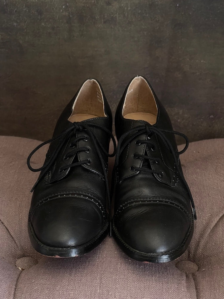 Vintage 90s y2k historically inspired black leather oxford heels with lace up detail, in front of historical painting background.