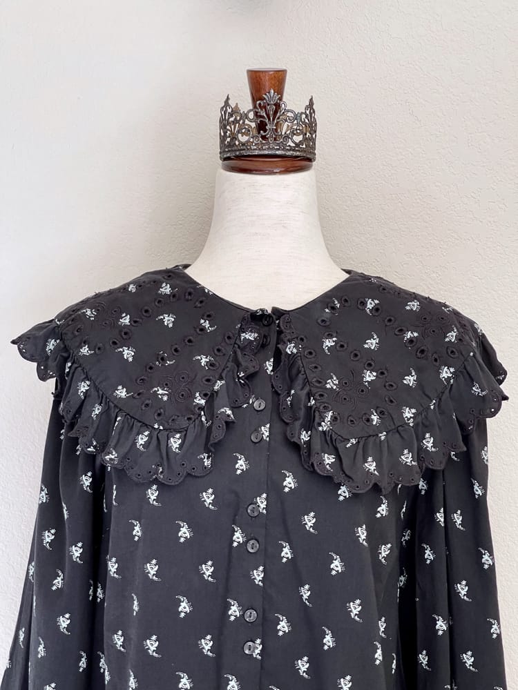 A black floral print historically inspired baroque blouse with large lace trimmed collar and long bishop sleeves is pictured on a mannequin from the front.