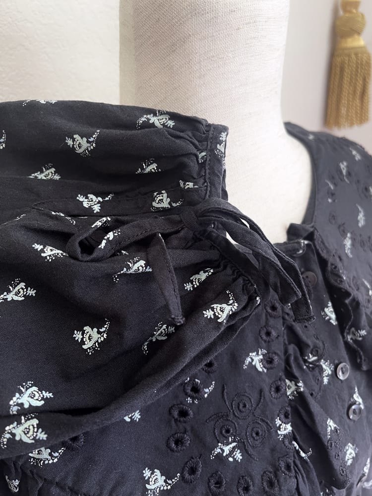 A black floral print historically inspired baroque blouse with large lace trimmed collar and long bishop sleeves is pictured on a mannequin, with up close sleeve detail.