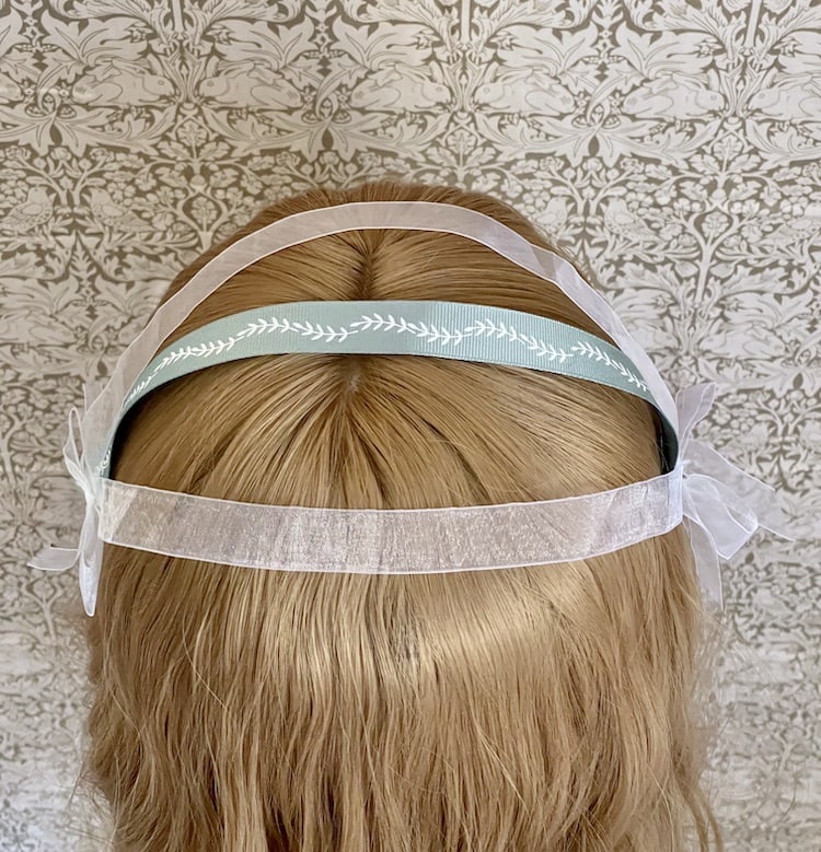A Handmade historically inspired regency era ribbon headdress in sage green with bow accents on a mannequin.