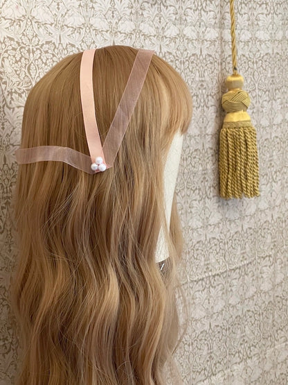 A handmade historically inspired regency era headdress in peachy pink with pearl accent is pictured on a mannequin.