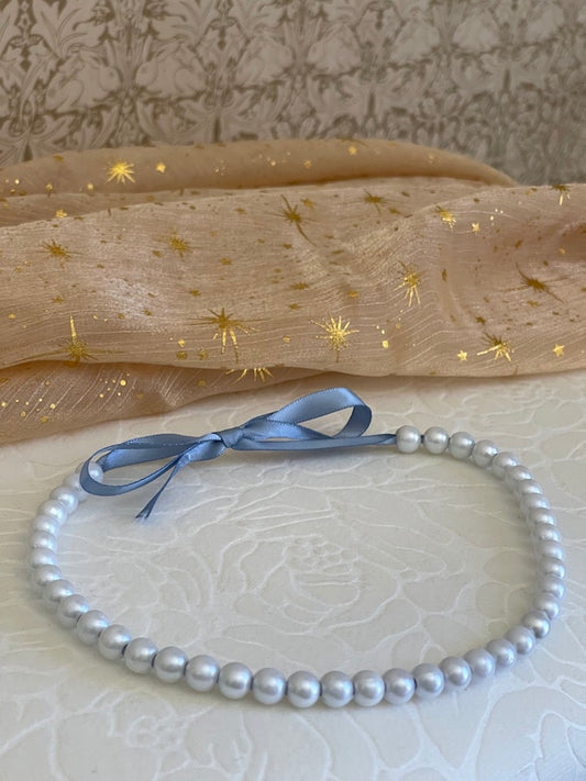 A handmade historically Inspired regency era pearl beaded choker necklace in cornflower blue on a floral puff.