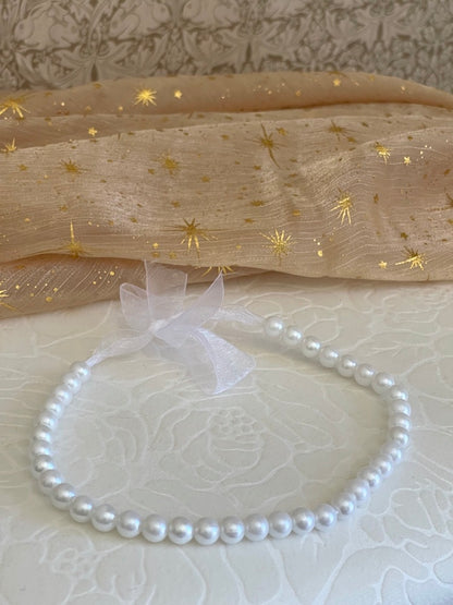 A Handmade historically inspired Regency inspired white pearl beaded ribbon choker necklace is pictured on a floral puff with a celestial background.